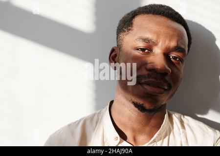 Portrait of African handsome man looking at camera standing against the white wall Stock Photo