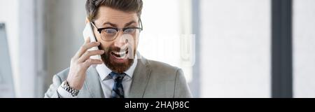 Excited businessman talking on mobile phone in office, banner Stock Photo
