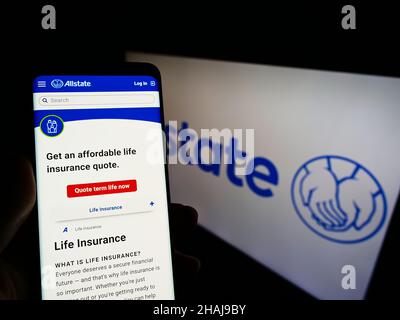 Person holding smartphone with website of US insurance company The Allstate Corporation on screen with logo. Focus on center of phone display. Stock Photo