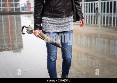 Woman holding folded umbrella and walking on city street in rain. City life and fashion accessory Stock Photo