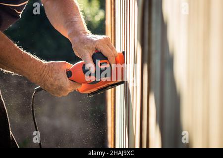 Sander in hands. Sanding wooden picket fence. Electric vibrating power tool grinder Stock Photo