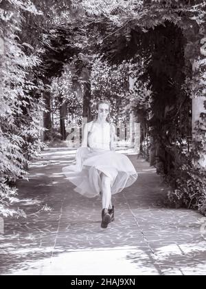 A lady with pigtails in light tulle skirt and rough boots is jumping along a park alley. Black and white photo Stock Photo