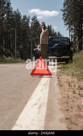 Triangle caution sign on road after car failure and ma speaking on smartphone, waiting for repair service. Stock Photo