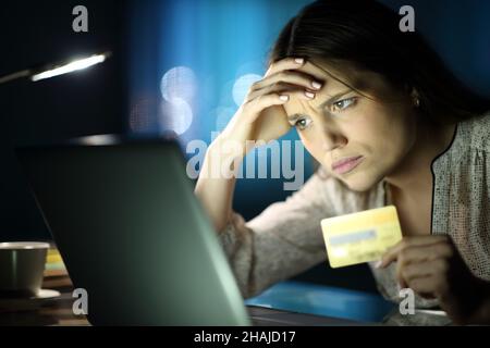 Worried woman in the night buying online with credit card and laptop at home Stock Photo