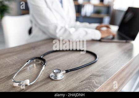 Stethoscope and background doctor using laptop at desk in clinic working on computer at office, cropped Stock Photo