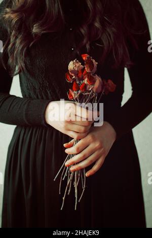Conceptual Young girl in black vintage dress and dried flowers Stock Photo