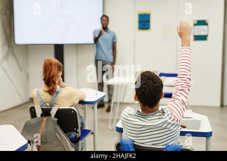 Back view portrait of African-American child raising hand in classroom, copy space Stock Photo