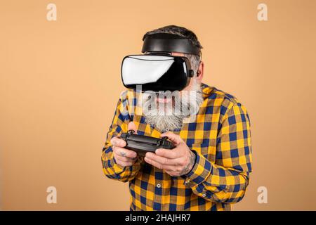 Bearded man playing video games on yellow background. Asian hipster man holding suit pad having fun, half-length shot. Stock Photo