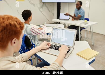 High angle view at red haired teenage boy using laptop in coding class for children, copy space Stock Photo