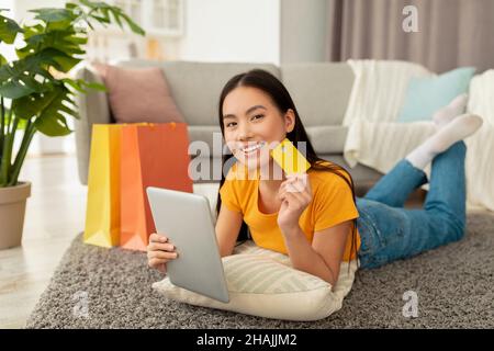 Online purchases concept. Positive asian woman shopping on internet using digital tablet and holding credit card Stock Photo