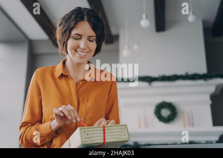 Attractive brunette Italian woman unpacking Christmas present gift box with red bow at home Stock Photo