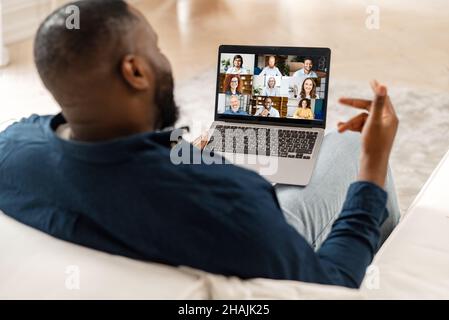 Brainstorming and virtual discussing with work group. African-American guy using laptop for video meeting with diverse colleagues, black freelancer involved online webinar,talk online with many people Stock Photo