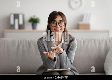 Portrait of positive middle eastern female psychologist talking to camera and taking notes during therapy session Stock Photo