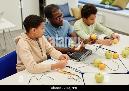 High angle portrait of young African-American teacher working on science experiments with diverse group of children Stock Photo