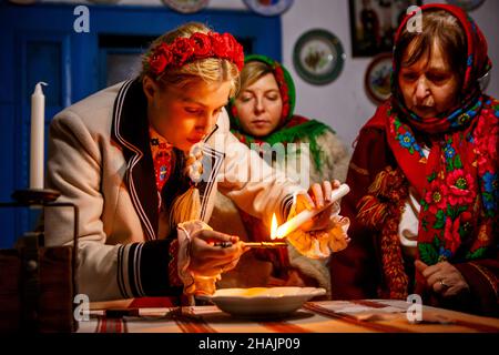 Non Exclusive: UZHHOROD, UKRAINE - DECEMBER 10, 2021 - A woman pours wax into the water as part of a fortune-telling ritual the Andriivski Vechornytsi Stock Photo