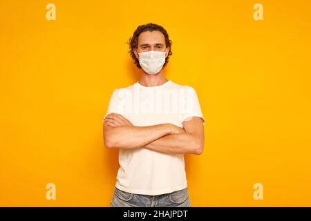 man in protective medical mask and casual clothes crossed his arms over his chest as sign of dissatisfaction isolated on yellow background. concept of people, medicine, protection from covid19 virus. High quality photo Stock Photo