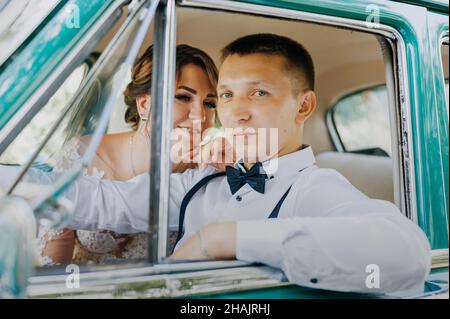 Gorgeous stylish blonde bride posing in retro green car with groom. The bride and groom are sitting inside the retro car. Wedding, bride and groom Stock Photo