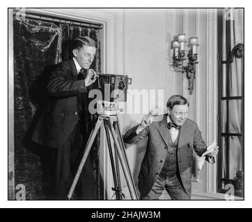 1900s Early Cinematography Vintage Movie Film Making. Two men using a 35mm hand crank silent movie film camera on a tripod indoors. Director with shooting film script calling ‘Action’  Detroit Publishing Co. publisher. USA America  [between 1908 and 1920] Cinematography Photography 'Le Parvo' /'J. Debrie, Paris' on manufacturers plate on 35 mm hand cranking movie film camera. Stock Photo