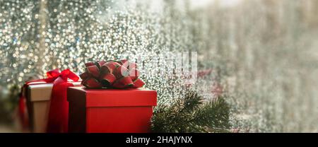 Christmas gift boxes with red ribbon on a window sill. Xmas garland decoration, raindrops on the glass, rainy day. Greeting card template, banner, cop Stock Photo