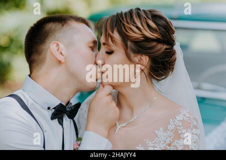 Just married wedding couple is standing near the retro vintage car in the park. Summer sunny day in forest. bride in elegant white dress with bouquet Stock Photo