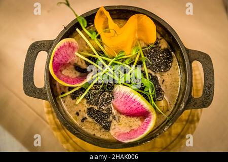 Black truffle lies in thin slices on a creamy base in a cast-iron pot at a bistro in Aups, Var department, France; watermelon radish, pea shoots and a curl of carrot garnish the dish. Stock Photo