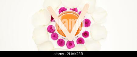 Jar of wax with wooden sticks, pink flowers, and white petals on white background. Concept of depilation. Flat lay top view Stock Photo
