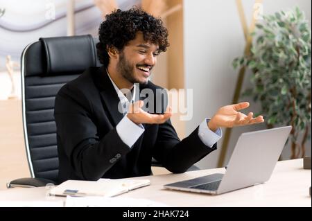 Happy attractive successful Indian businessman, manager or business coach in stylish suit, communicates with colleagues, conducts virtual business trainings, brainstorming works remotely, smiling Stock Photo