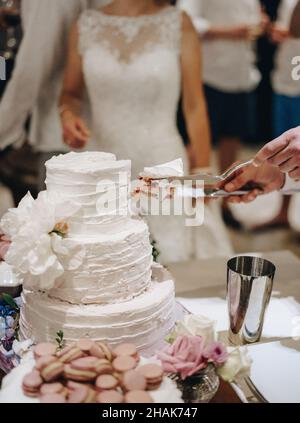 Cutting a white wedding three-tiered cake Stock Photo