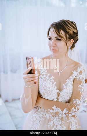 Excited bride young woman in white wedding dress doing selfie shot on mobile phone pointing thumb on herself isolated on blue turquoise background Stock Photo