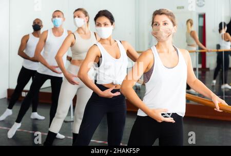 Group of men and women in protective masks practicing at the ballet barre Stock Photo