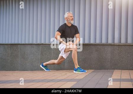 Active middle aged sportive man in sports clothing stretching his legs, warming up and exercising outdoors Stock Photo