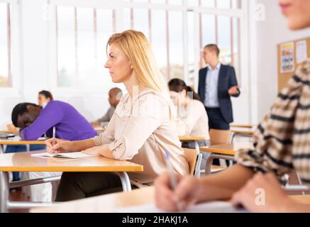 Portrait of focused female sitting at desk studying in classroom with colleagues Stock Photo