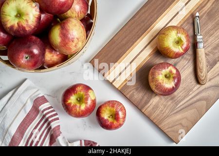 Cortland apples on a cutting board with a peeler and more apples in a basket Stock Photo