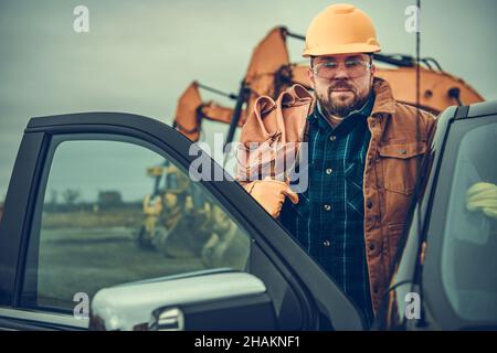Caucasian Construction Contractor Worker in His 30s with Tool Belt on His Shoulder Staying Next to His Truck. Stock Photo