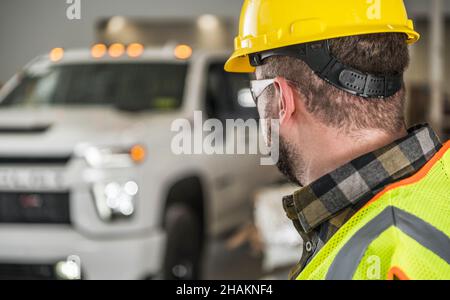 Construction Worker in Yellow Hard Hat and Eyes Protection Glasses Looking at His Brand New Commercial Pickup Truck Stock Photo