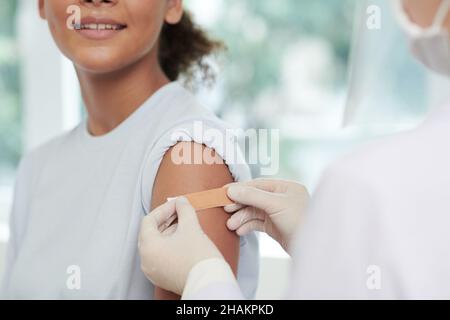 Close-up image of nurse sticking adhesive plaster on arm of teenage girl after injecting vaccine against covid-19 Stock Photo