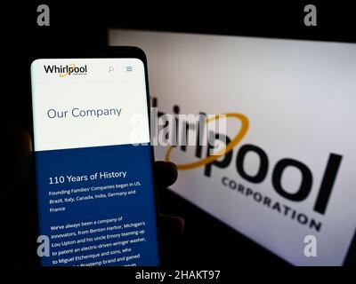 Person holding cellphone with website of US home appliances company Whirlpool Corporation on screen with logo. Focus on center of phone display. Stock Photo