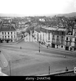 Quiet street scene below Chateau Saint-Germain-en-Laye , early 1945.The photographer aimed his camera down onto the quiet streets while visiting Chateau Saint-Germain-en-Laye. The view goes across an intersection to look down Rue du Vieil Abreuvoir.  There are pedestrians, including several walking down the center of the roadway. The three to five story buildings are 19th Century. The base of the photo depicts a wall and depression that are part of the moat of the palace. The only vehicle in view is a parked military jeep. There is a three-story ad for Aux Galeries Lafayette painted on a wall. Stock Photo