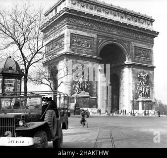 Paris Arc de triomphe with US Jeep and Navy personnel, 1945. In view is the Neoclassical Arc de Triomphe (1836) and the circular Place de l Etoile taken from Avenue Marceau near the end of World War II. The jeep sits with three American sailors waiting for the fourth who is out of the vehicle taking the photo.  The roadway contains one bicyclist and one military truck. A man is pulling a primitive two-wheel cart in the roadway. In the photo are numerous visitors beneath the Arc. A kiosk promotes the Loterie Nationale. Vintage streetlights are in view. Stock Photo