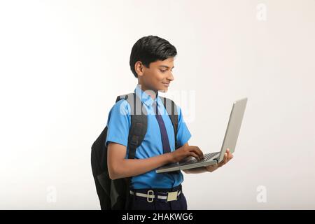 Indian school boy in uniform and using laptop on white background. Stock Photo