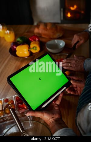 Hands of multi-cultural elderly male using tablet in modern kitchen. Happy couple cooking healthy meal. Stock Photo
