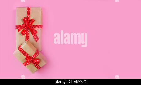 Wrapped craft paper boxes with gifts decorated with red bow on pink background Stock Photo