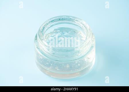 Transparent gel jar on blue background. Cosmetic gel with bubbles texture close up. Clear colored liquid beauty product sample. Stock Photo