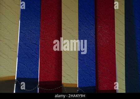 Vertical fabric blinds of blue, yellow and red colors installed on the window Stock Photo
