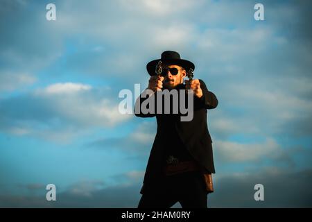 Sheriff or cowboy in black suit with vintage pistol revolver and marshal ammunition. American western Sheriff. Wild west with cowboy. Stock Photo