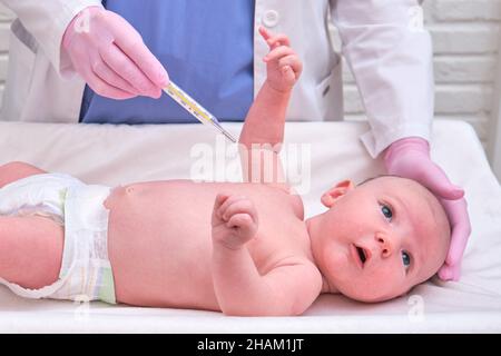 Doctor checks the temperature of the newborn baby with a thermometer. A nurse in uniform measures the child fever with a thermometer Stock Photo