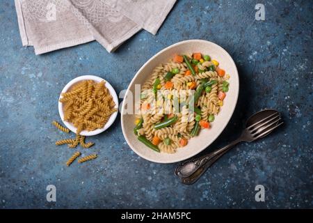 Top view of italian rotini pasta with green peas and beans, corn and carrot for vegetarian and dieting nutrition on blue concrete background Stock Photo