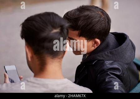Men sitting on bench and looking at cell phone Stock Photo