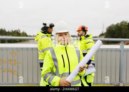 Engineers in reflective clothing standing on bridge with blueprints Stock Photo