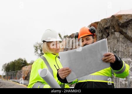 Engineers in reflecting clothing looking at blueprints Stock Photo